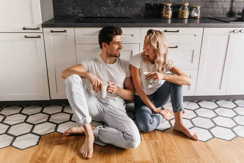 Young couple sits on unique kitchen flooring enjoying a cup of coffee together.