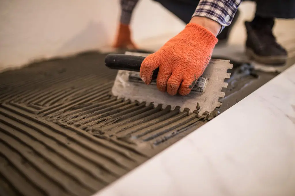 Troweling mortar onto a concrete floor in preparation for laying white floor tile during a Chicago home remodel.