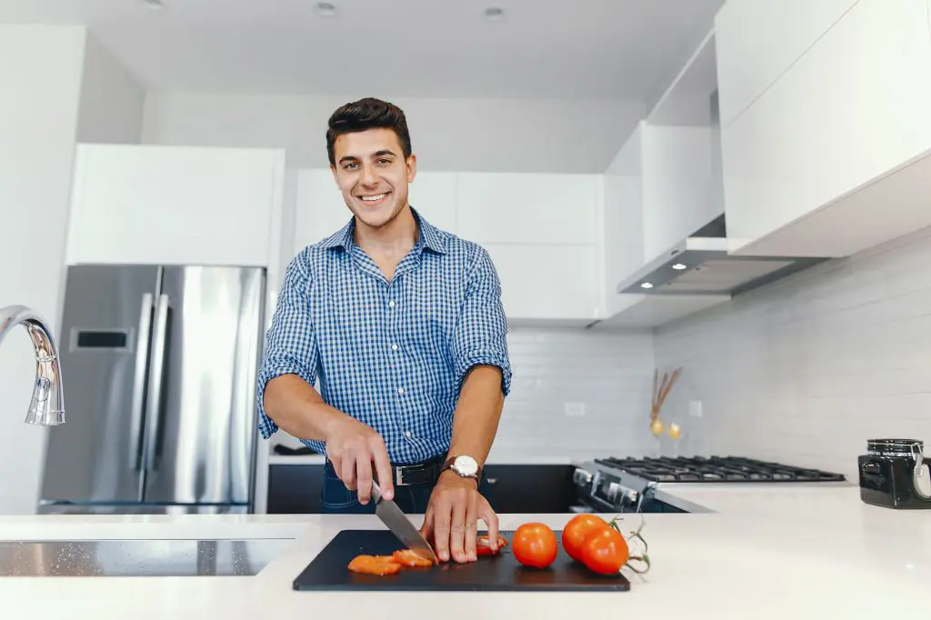 A man cuts vegetables on his kitchen counter in a small, modern kitchen with a thoughtfully designed layout.