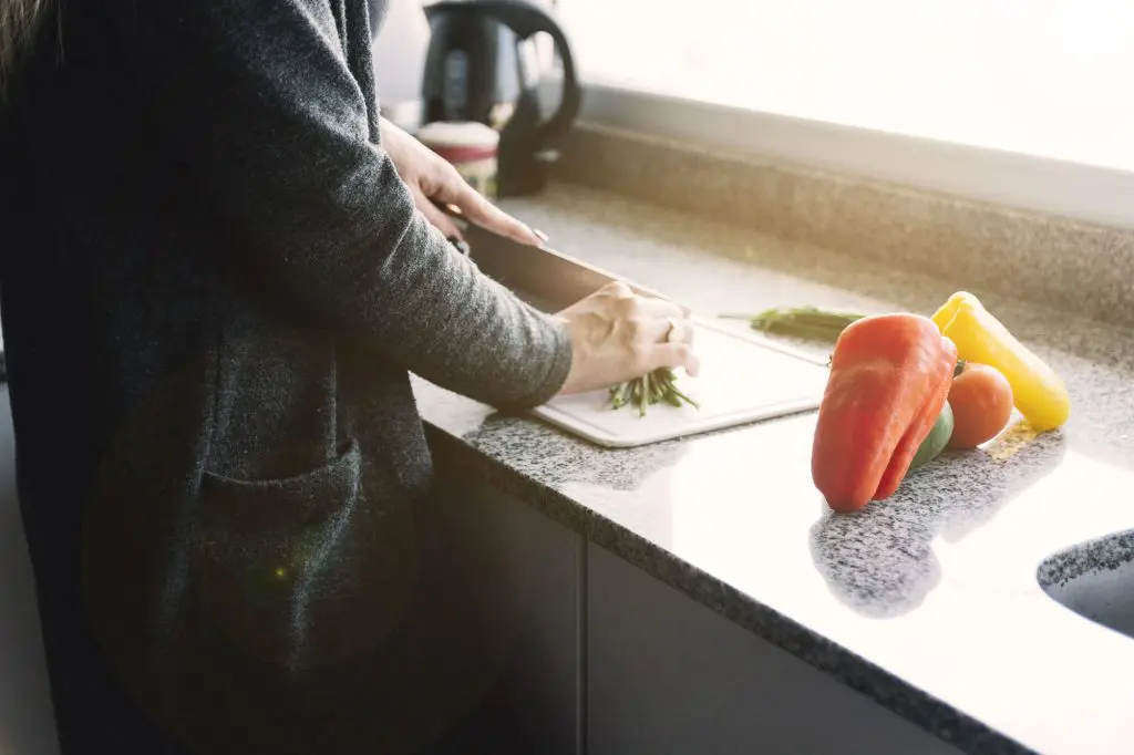 Close up shot of a woman's hands chopping vegetables at her spacious kitchen counter.
