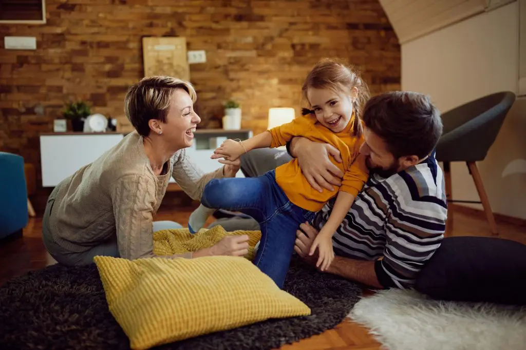 A family with a young girl laugh and play in the finished basement of their home.