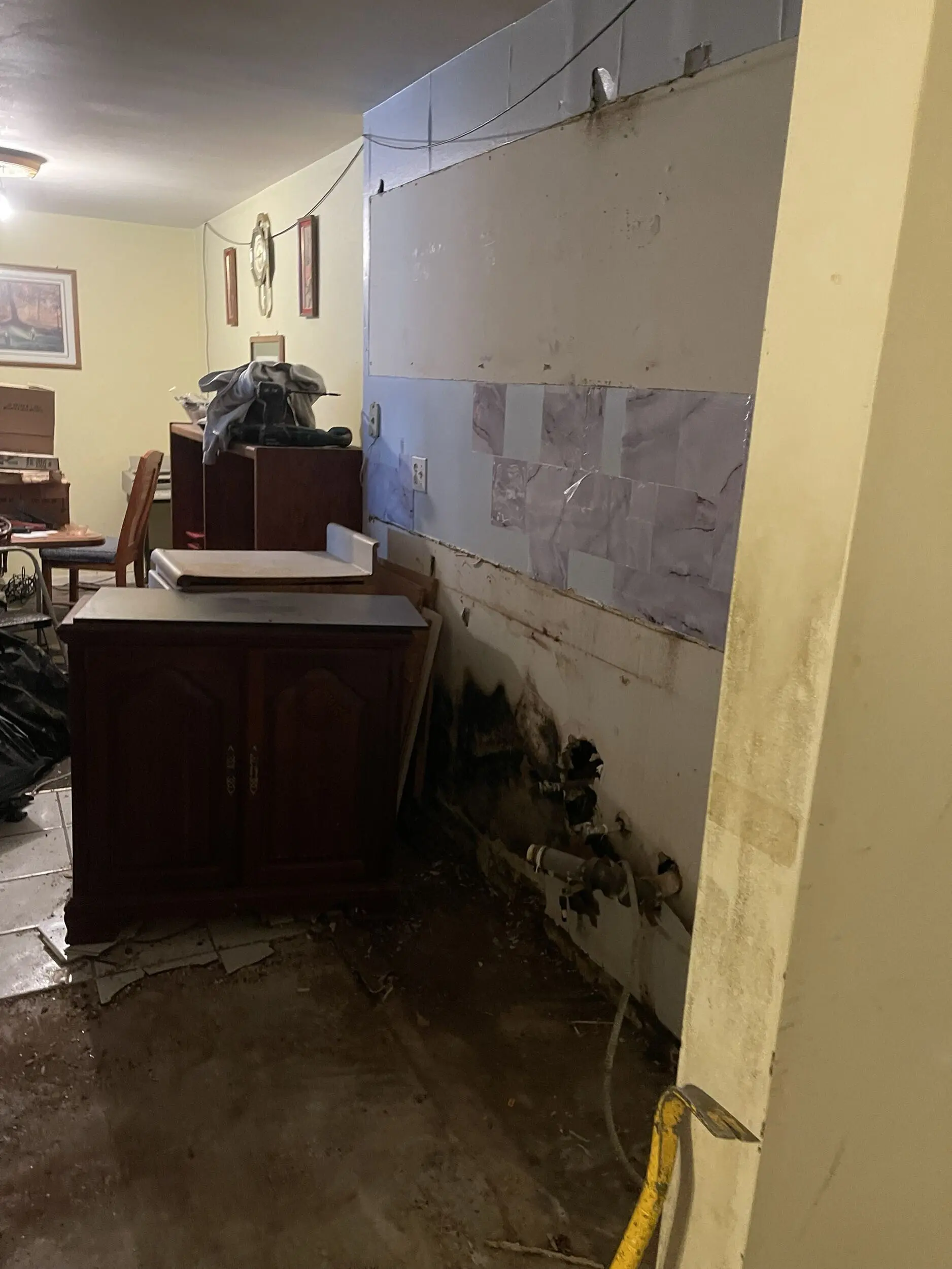 Water damage and exposed pipes behind removed wall tile