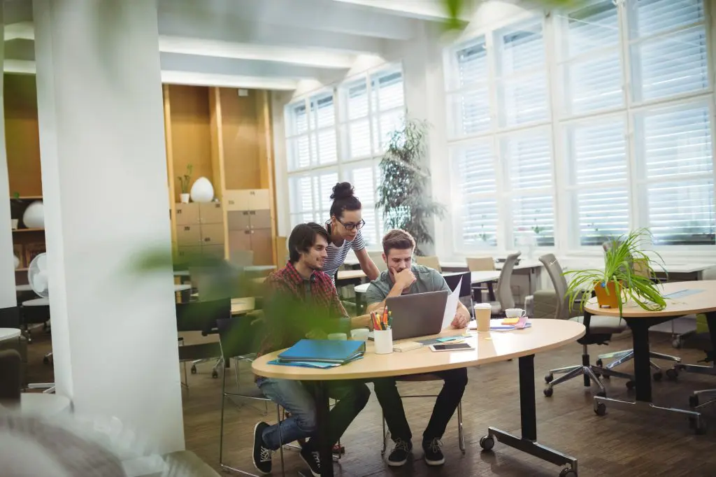 A group of business executives discuss a business matter over laptop at their desk in a shared workspace.