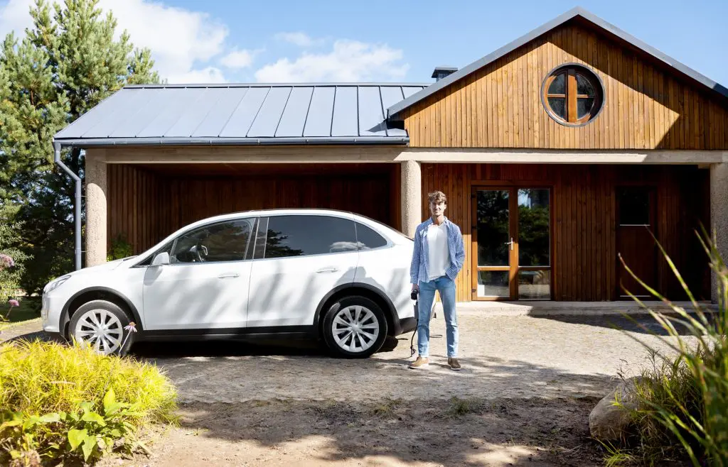 A man stands outside of his open garage with his electric car.