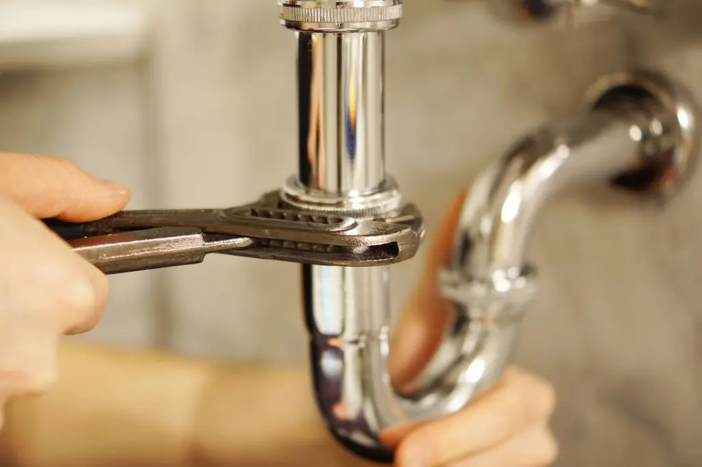 A professional plumber with a wrench checking a pipe.
